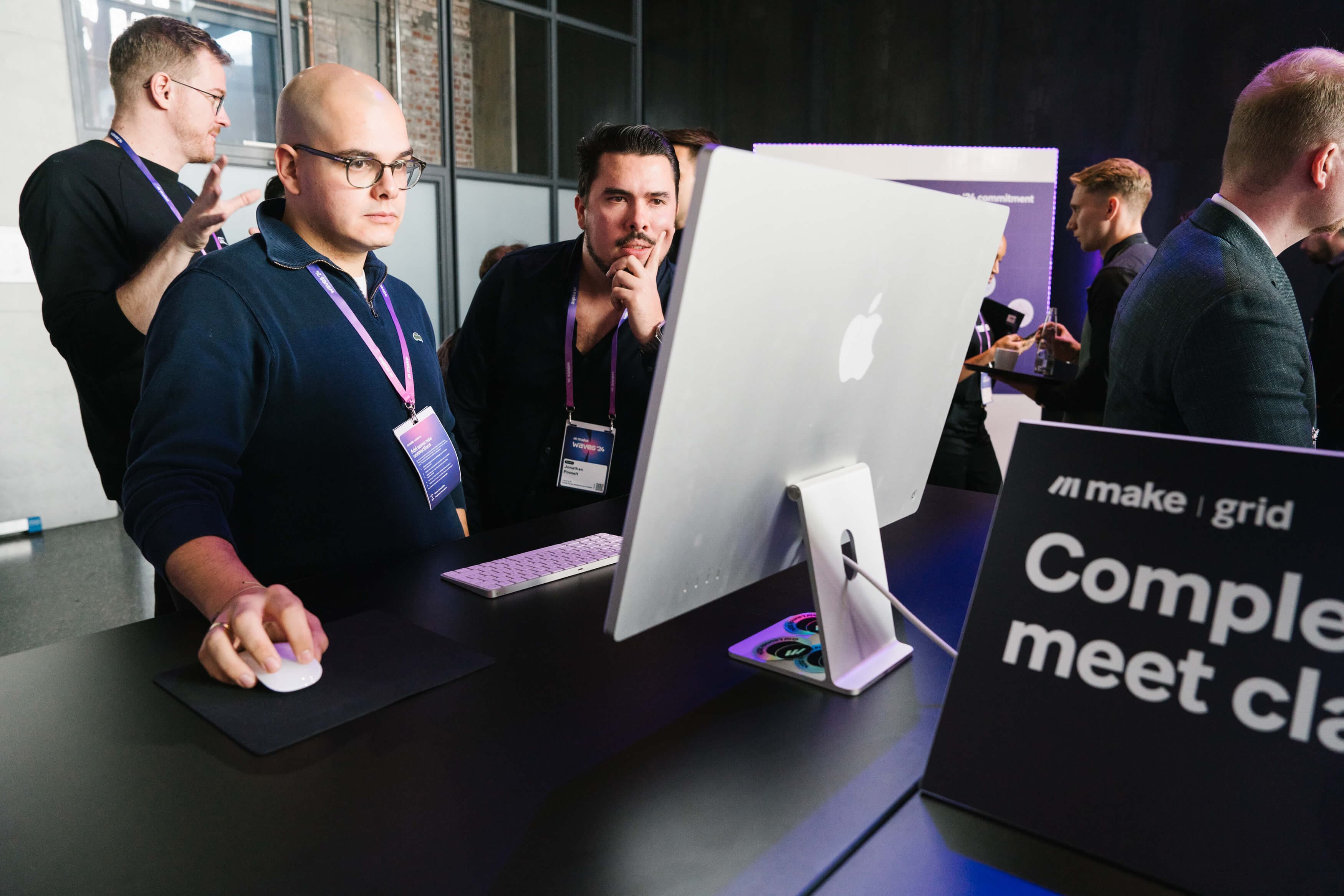 A Waves attendee wearing a purple lanyard stands at a computer and uses a mouse while a colleague looks on